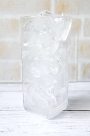 Transparent glass fill with ice cube on white wooden background.の写真素材