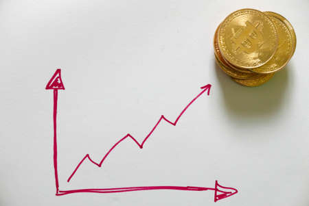 A stack of golden bitcoin replica on white paper written with red graph up and down. Business and finance concept.の写真素材