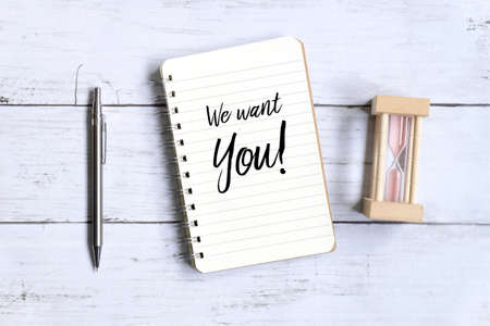 Top view of pen,hourglass and notebook written with 'WE WANT YOU!' on white wooden background.の写真素材