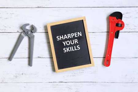 Top view of cutter,wrench and blackboard written with 'SHARPEN YOUR SKILLS' on white wooden background.の写真素材