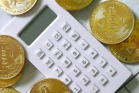 Golden Bitcoin replica and white calculator. Business and finance concept.の写真素材