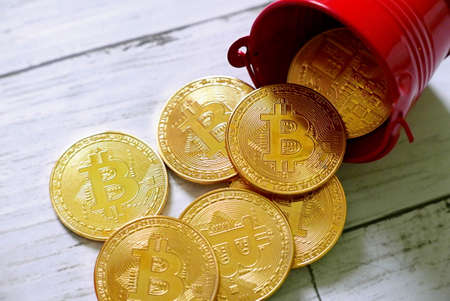 Golden Bitcoin replica fall from red pile on white wooden background. Business and finance concept.の写真素材