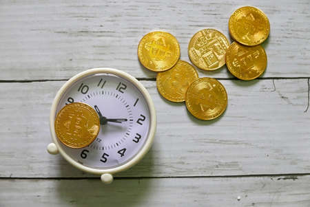 A golden replica of bitcoin with clock on white wooden background.Business and finance concept.の写真素材