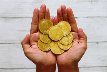 A hand holding golden bitcoin replica on white wooden background. Business and finance concept.の写真素材