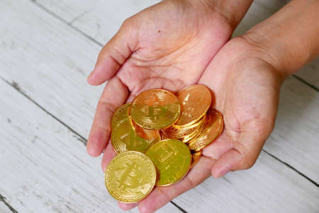 A hand holding golden bitcoin replica on white wooden background. Business and finance concept.の写真素材