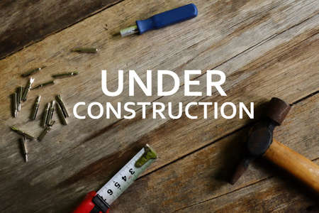 Business concept. Hammer, measuring tape, screw driver with UNDER CONSTRUCTION' words on wooden...