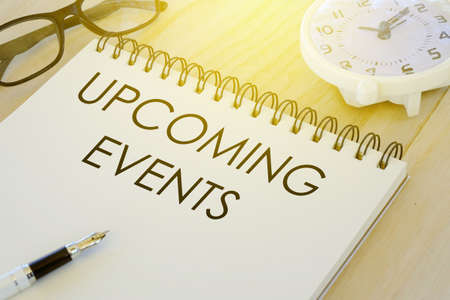 Sunglasses,pen,table clock and notebook written with Upcoming Events on wooden background.