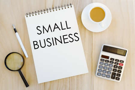 Top view of magnifying glass,pen,a cup of coffee,calculator and notebook written with Small Business...