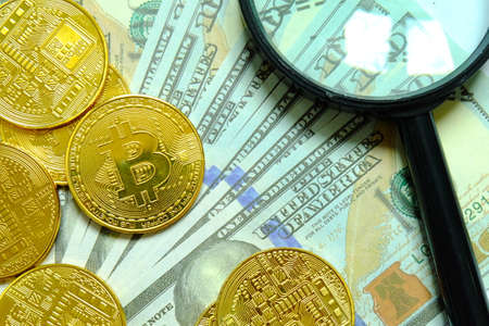 Business and finance concept.Golden Bitcoin replica with magnifying glass on dollar bills or bank...