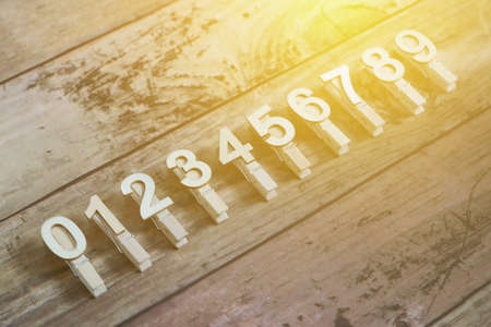 Clothpin with number of 0,1,2,3,4,5,6,7,8, and 9 in a row with sun flare and wooden background.