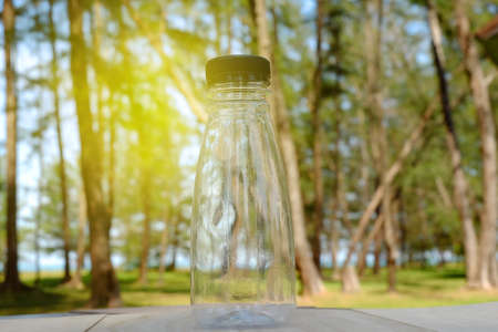 Selective focus an empty transparent bottle with forest background and sun flare.