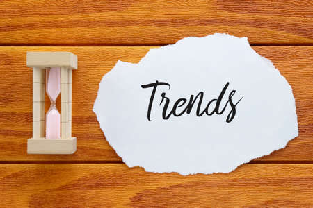 Top view of sand clock and piece of paper written with Trends on wooden background.の写真素材