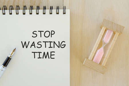 Business and finance concept. Top view of sand clock pen and notebook written with Stop Wasting Time.の写真素材