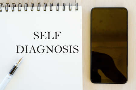 Health concept.Top view of mobile phone,pen and notebook written with Self Diagnosis.の写真素材