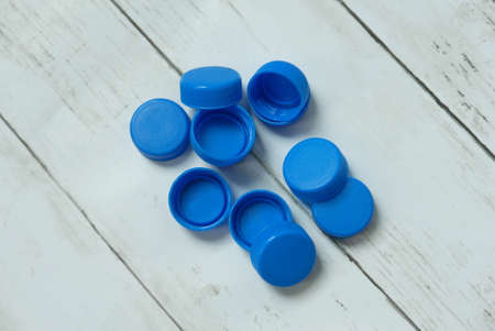 Selective focus and close up of blue plastic bottle cap on white wooden background.