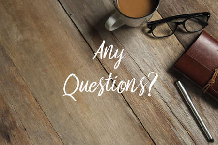 Top view of a cup of coffee,glasses,notebook and pen on wooden background written with Any Questions?の写真素材