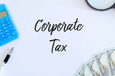 Top view of pen,calculator,magnifying glass and dollar bank note on white background written with Corporate Tax.の写真素材