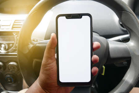 Close up of hand holding phone with white screen inside a car. Smartphone with mockup on background of car dashboard.の写真素材