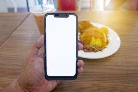 Close up of hand holding phone with white screen. Smartphone with mockup on background of cafeteria...