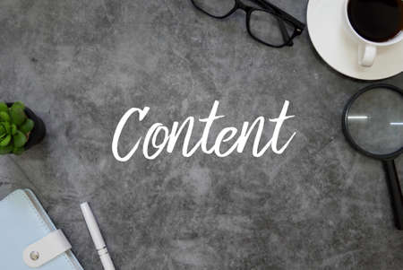 Top view of notebook,pen,plant,magnifying glass,coffee and glasses on grey grunge floor written with Content.の写真素材