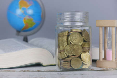 Selective focus of Gold coins, book, hourglass and globe. Finance and education concept.