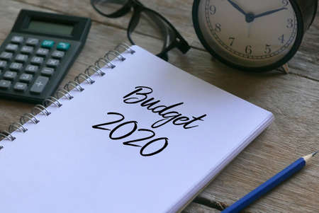 Calculator.glasses,clock,pencil and notebook written with Budget 2020 on wooden background.の写真素材
