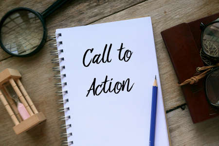 Top view of magnifying glass,sand clock,glasses,pencil and notebook written with Call to Action on wooden background.の写真素材