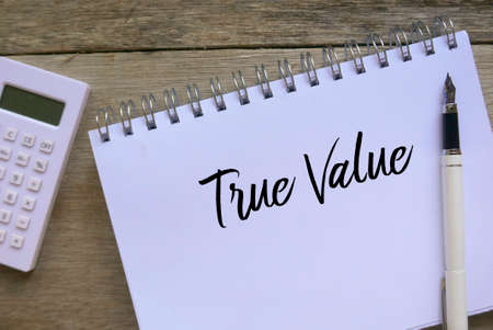 Top view of calculator,pen and notebook written with True Value on wooden background.の写真素材
