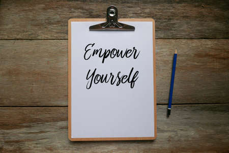Top view of pencil and clipboard with white paper written with Empower Yourself on wooden...