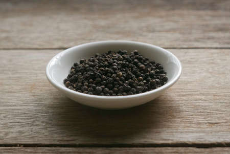 Black pepper in a white plate on wooden background.