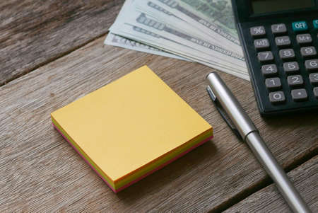 Dollar bank notes,calculator,pen and blank yellow sticky notes on wooden background. Copy space.の写真素材