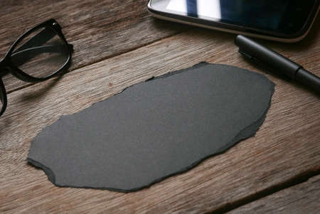 A glasses,mobile phone,pen and blank black paper on wooden background. Copy space.の写真素材