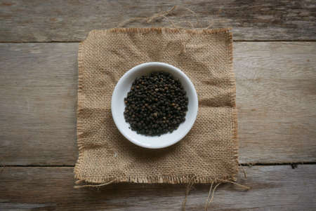 Black pepper in a white plate on rug sack on wooden background.の写真素材