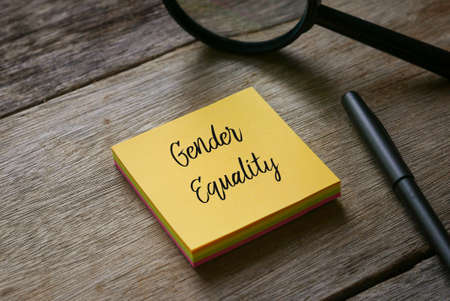 Magnifying glass,pen and yellow sticky notes written with Gender Equality on wooden background.の写真素材