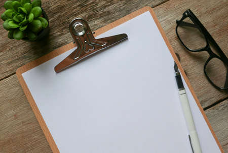 Writing board and white paper with stationery on wooden background. Copy space for text or logo.の写真素材