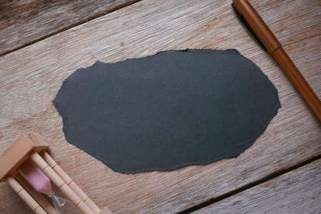 Pen,sand clock, and piece of empty black paper on wooden background.Copy space.の写真素材