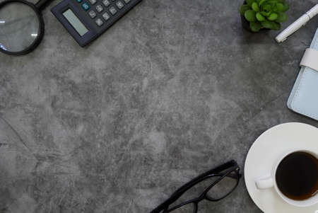 Top view of magnifying glass,calculator,plant,glasses and a cup of coffee on grey grunge floor. Copy space for text or logo.の写真素材