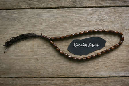Rosary beads and a piece of black paper written with Ramadan Kareem on wooden background.