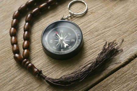Rosary beads and compass on wooden background.