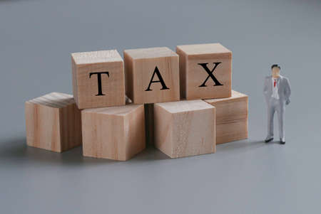Miniature people with wooden blocks written with TAX on grey background.の写真素材