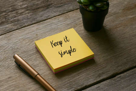 Pen, plant and yellow sticky notes written with Keep it simple on wooden background.