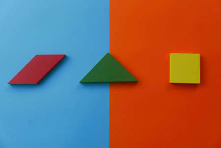 Top view of shapes of red parallelogram, green triangle and yellow square on two color background which are blue and red.の写真素材