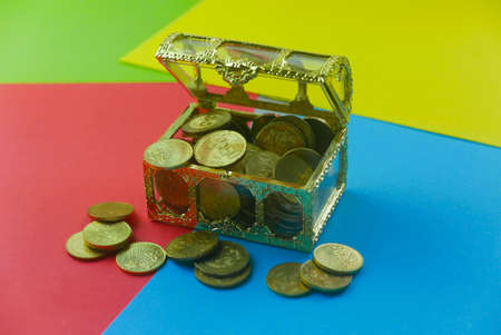 An open treasury chest full with gold coins on a four color background of green,yellow,red and blue.