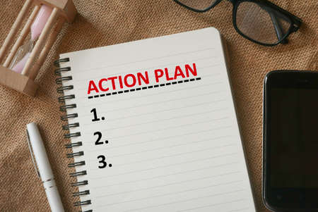 Top view of sand clock,glasses,mobile phone,pen and notebook written with list with numbering of Action Plan.の写真素材