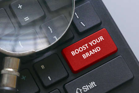 Magnifying glass on a computer keyboard with red button written with advice Boost your brand.の写真素材