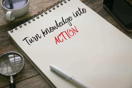 Selective focus of magnifying glass,coffee, mobile phone,pen and notebook written with Turn knowledge into action on wooden background.の写真素材