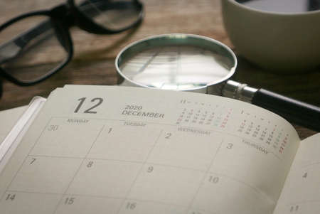Selective focus monthly planner in page December together with a cup of coffee,magnifying glass and glasses. December represent Q4 or quarter four in business.の写真素材