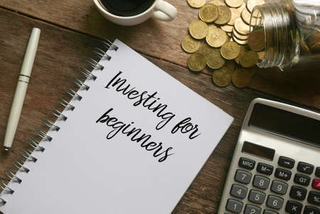 Selective focus of coffee,calculator,gold coins, pen and notebook written with Investing for beginners on wooden background.の写真素材