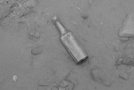 Selective focus of an old glass bottle covered with mud and water by the beach. Photo in black and white.の写真素材