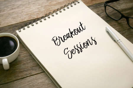 Selective focus of coffee,glasses,pen and notebook written with Breakout Sessions on wooden...